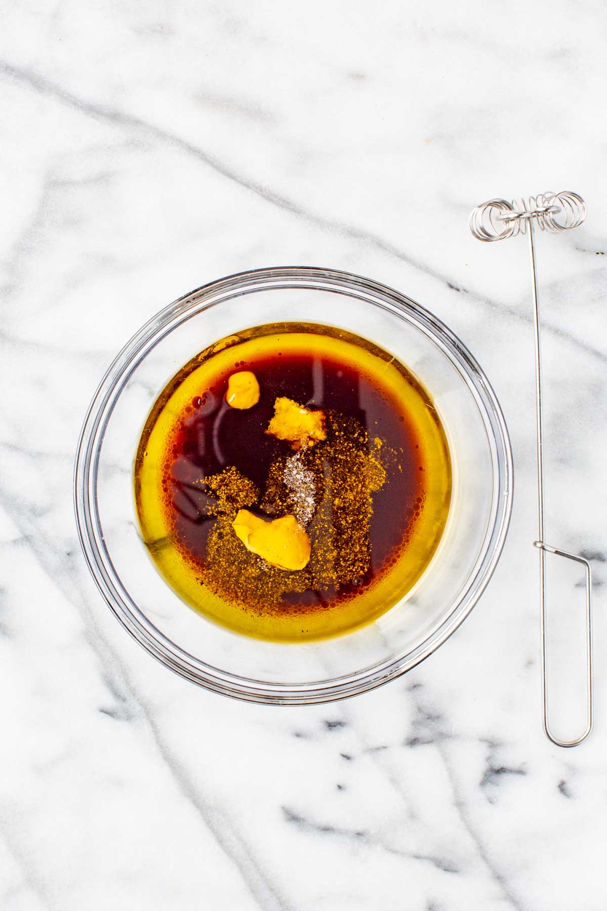 Unmixed balsamic vinaigrette ingredients in a glass bowl, including mustard, garlic, and seasonings, ready to be whisked.