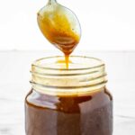 A spoon drizzling finished balsamic vinaigrette back into a glass jar with thick consistency.