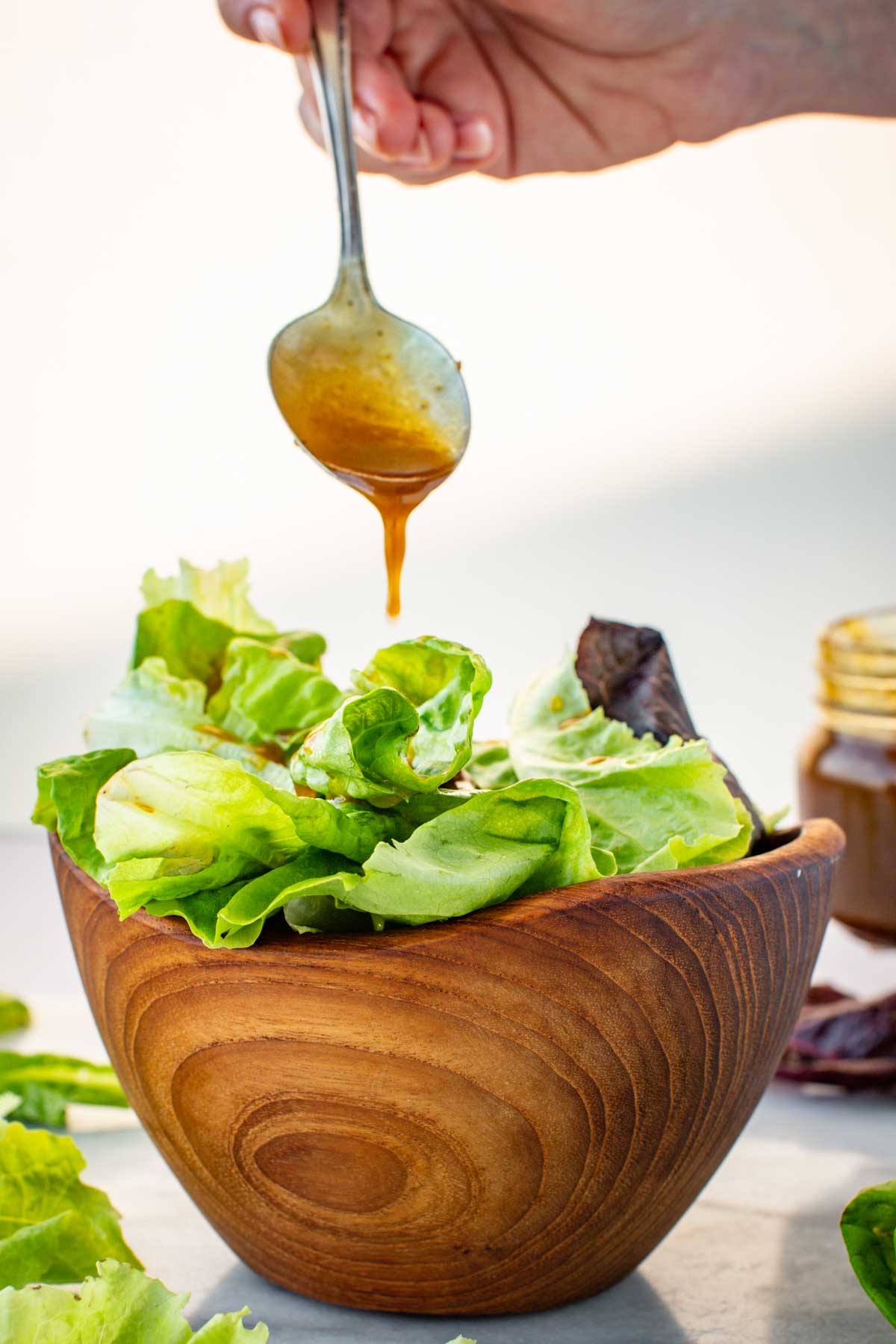 Close-up of balsamic vinaigrette being spooned onto a green salad in a rustic wooden bowl.