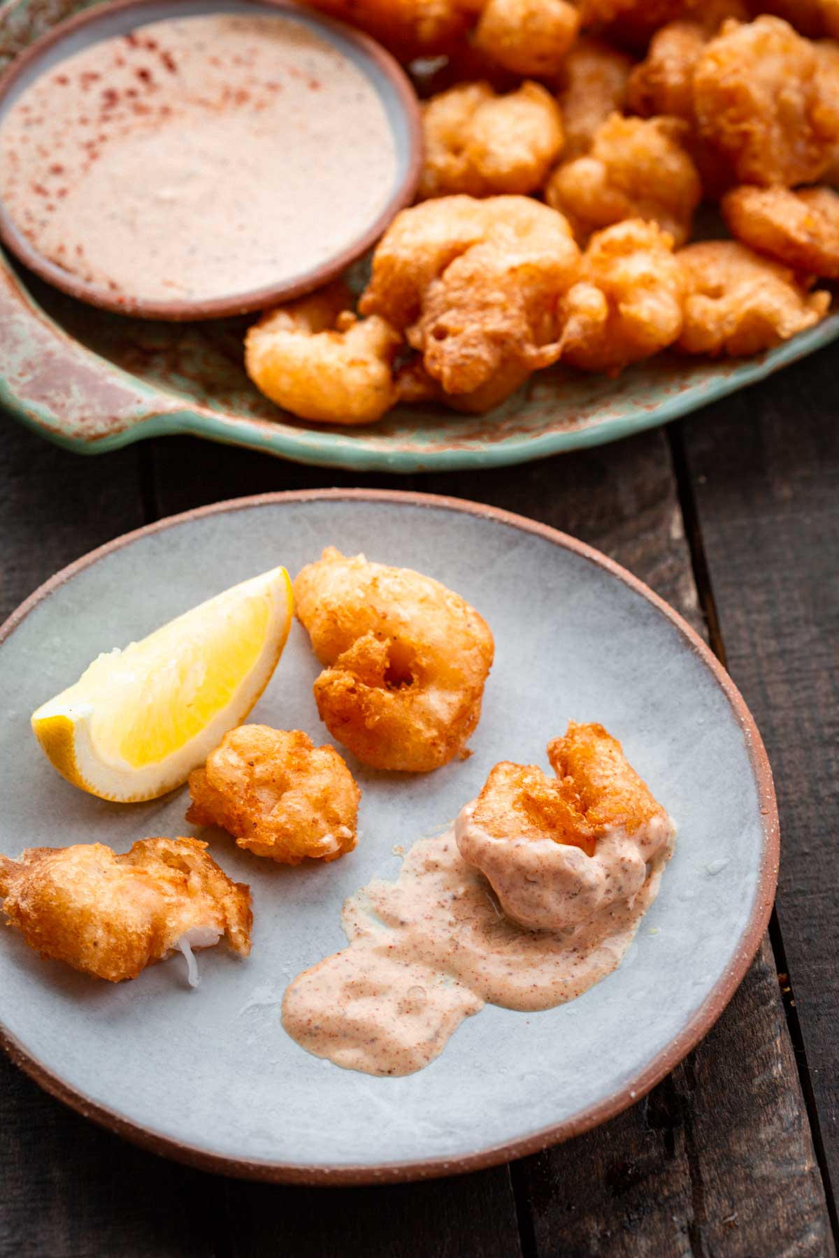 Small plate with a few shrimp, a lemon wedge, and dollops of dipping sauce, one shrimp partially coated.