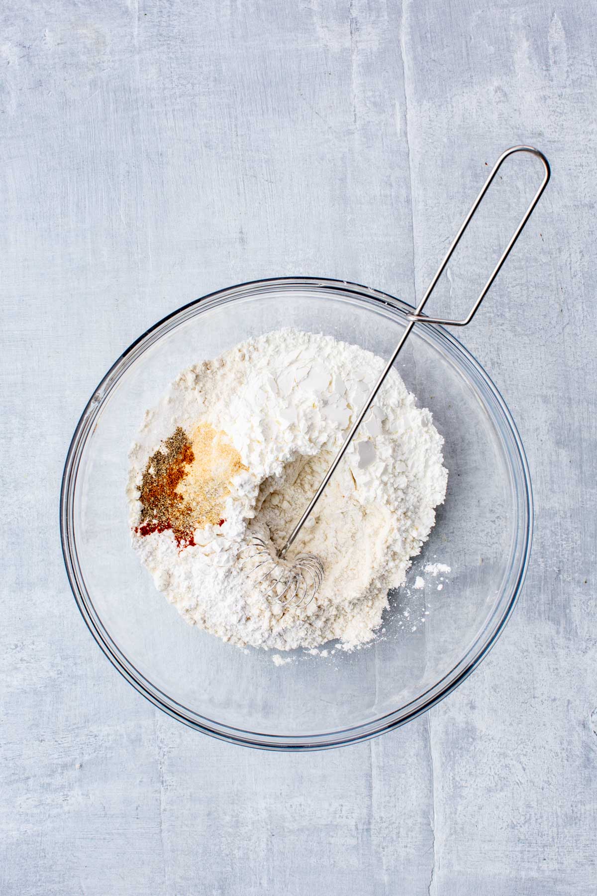Overhead view of flour and spices in a glass bowl with a whisk, ready to be combined for the beer batter.