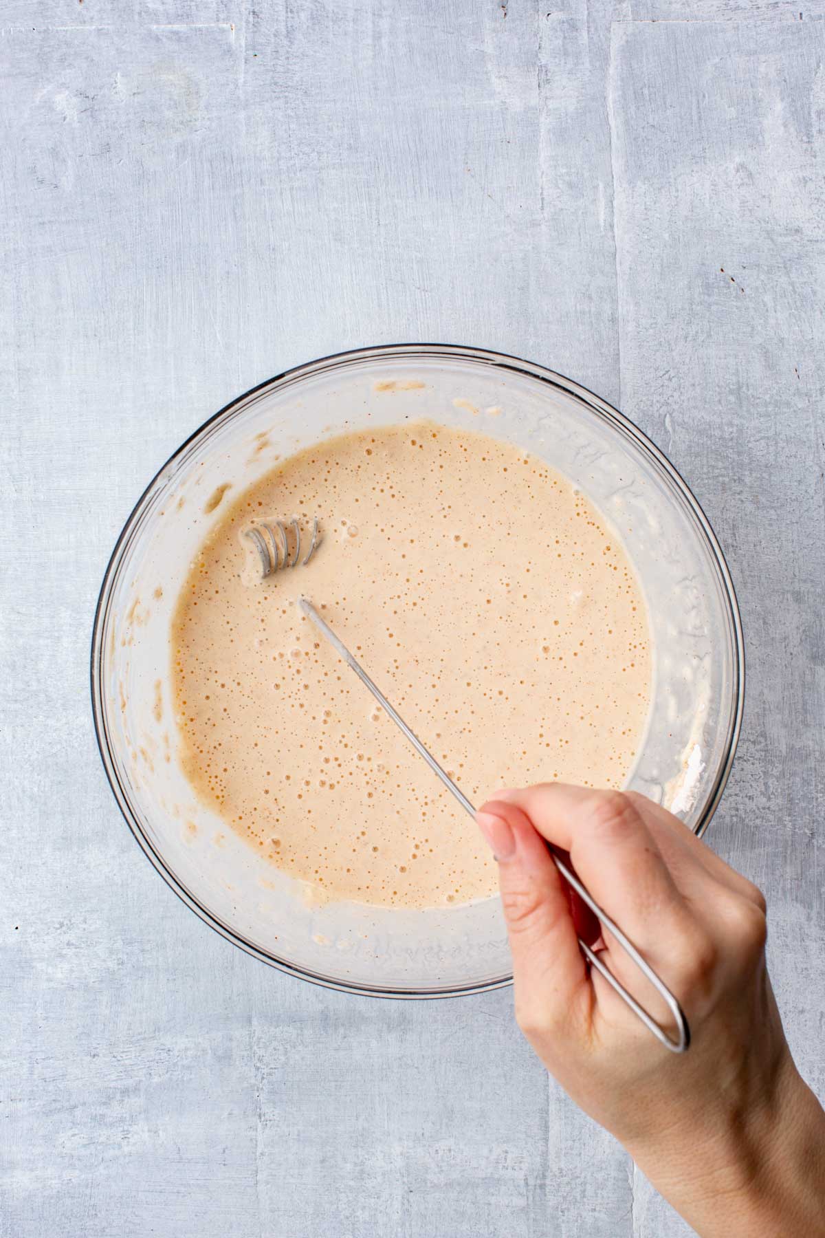 Whisk resting in a bowl of smooth, golden-hued beer batter after being fully mixed.