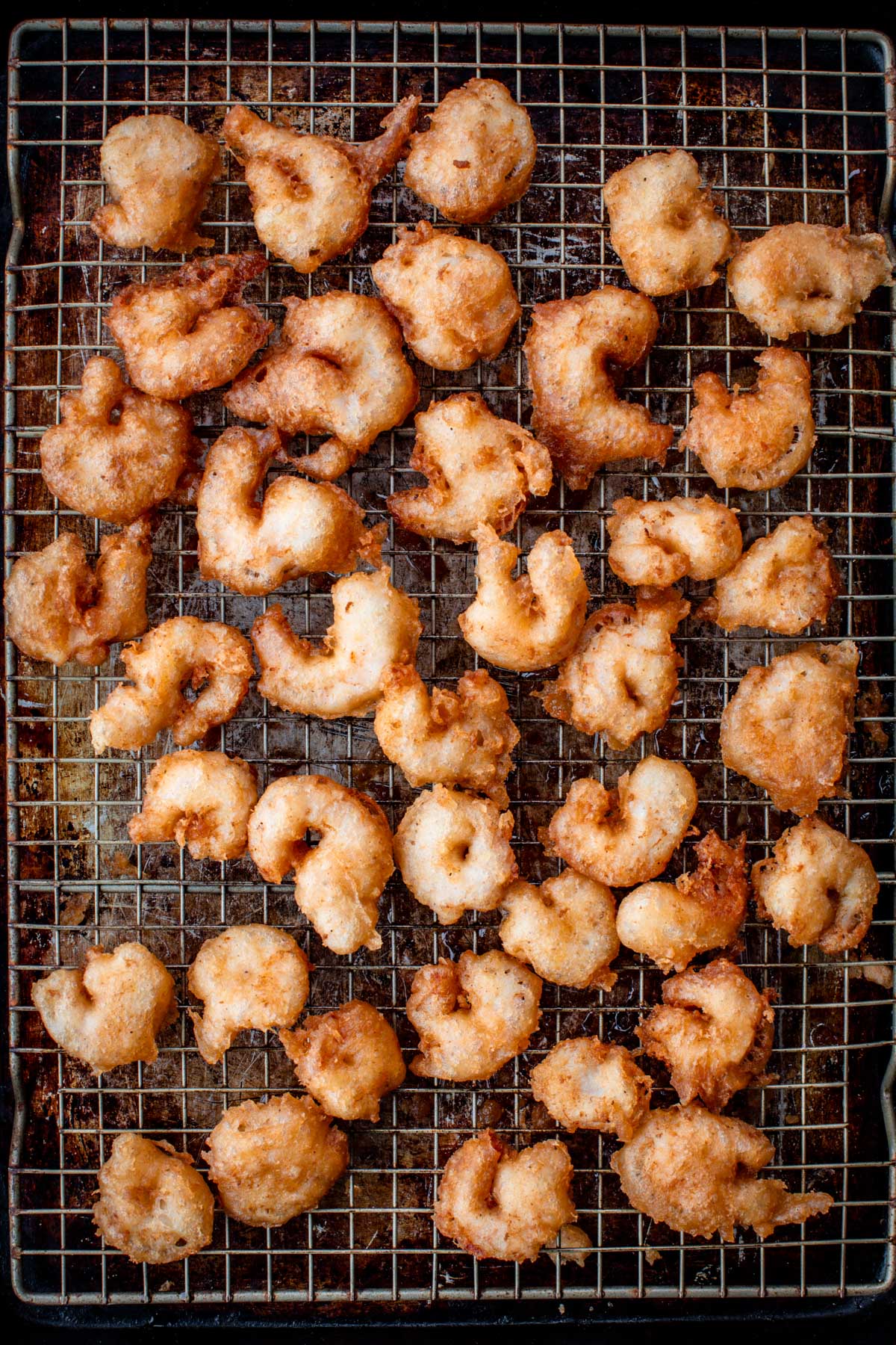 Dozens of golden, crispy beer-battered shrimp resting on a wire rack to drain after frying.