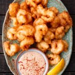 Close-up of crispy beer battered shrimp served on a rustic green platter with a ramekin of dipping sauce and a lemon wedge.