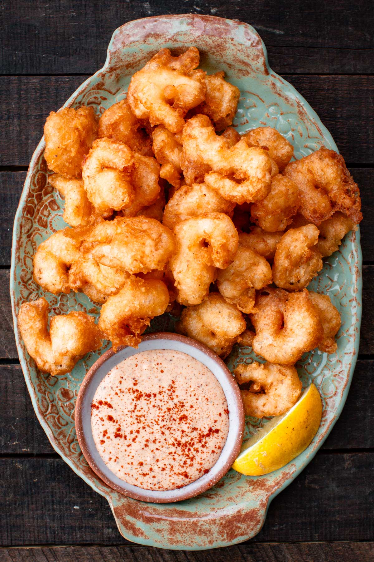 Close-up of crispy beer battered shrimp served on a rustic green platter with a ramekin of dipping sauce and a lemon wedge.