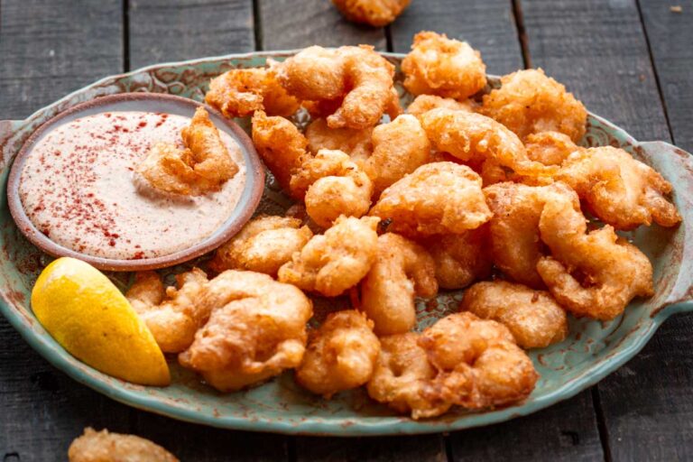 Close shot of shrimp being dipped into creamy, paprika-speckled sauce, highlighting the crisp texture.