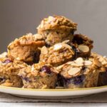 A pile of blueberry almond baked oatmeal cups stacked on a striped plate, topped with toasted almond slices.