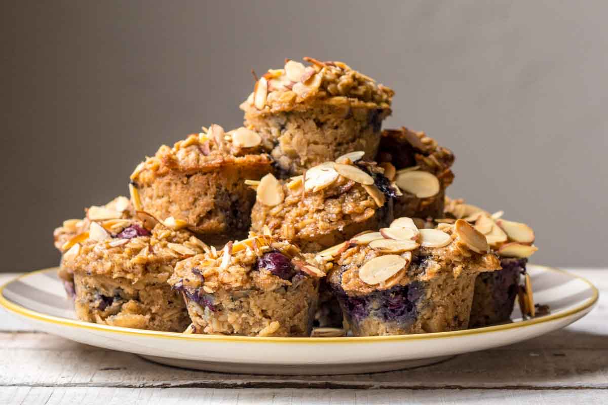 A pile of blueberry almond baked oatmeal cups stacked on a striped plate, topped with toasted almond slices.