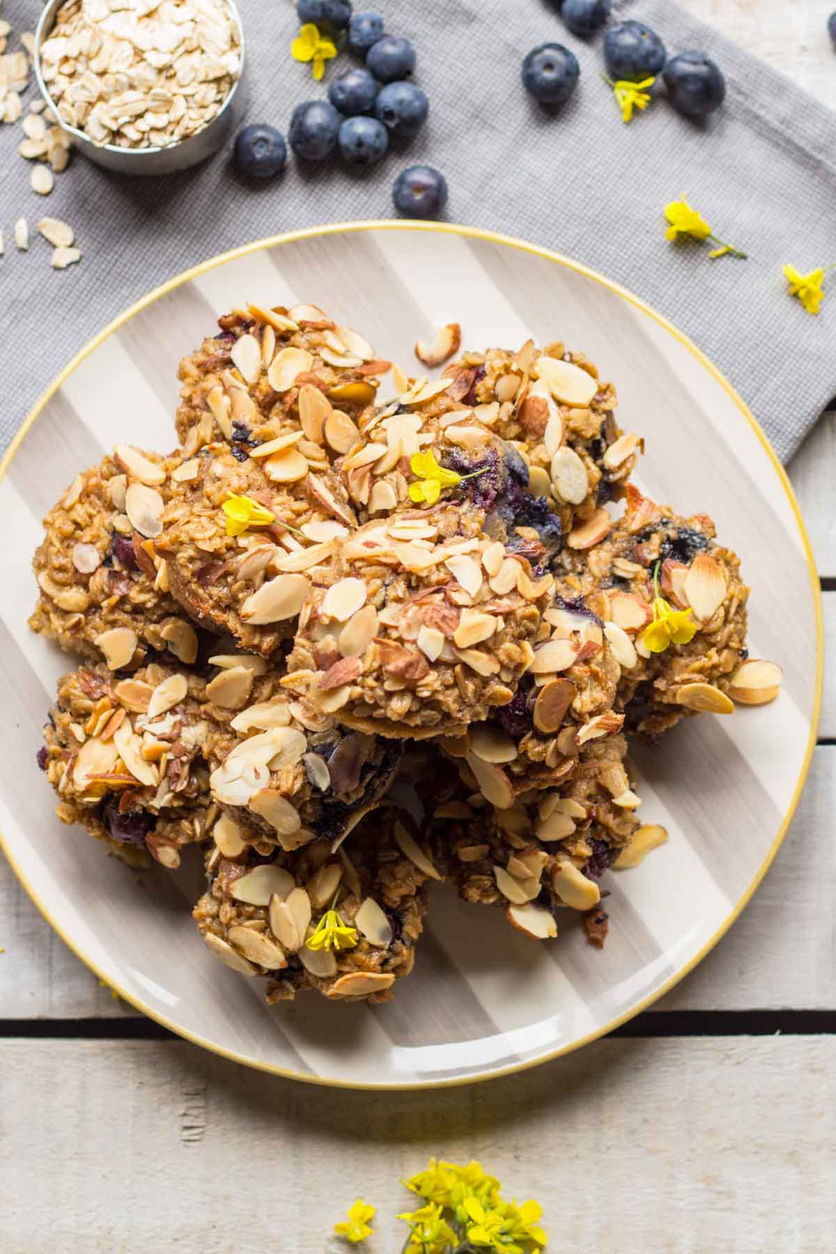 Top-down view of oatmeal cups on a striped plate, garnished with sliced almonds and scattered blueberries and oats.