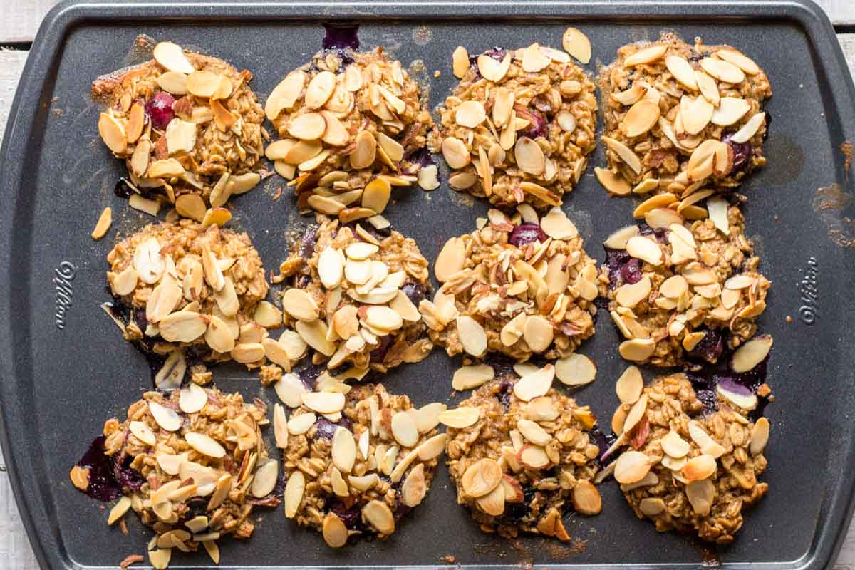 Overhead shot of a muffin tin filled with baked blueberry almond oatmeal cups, showing a full batch with toasted tops and berry juices.