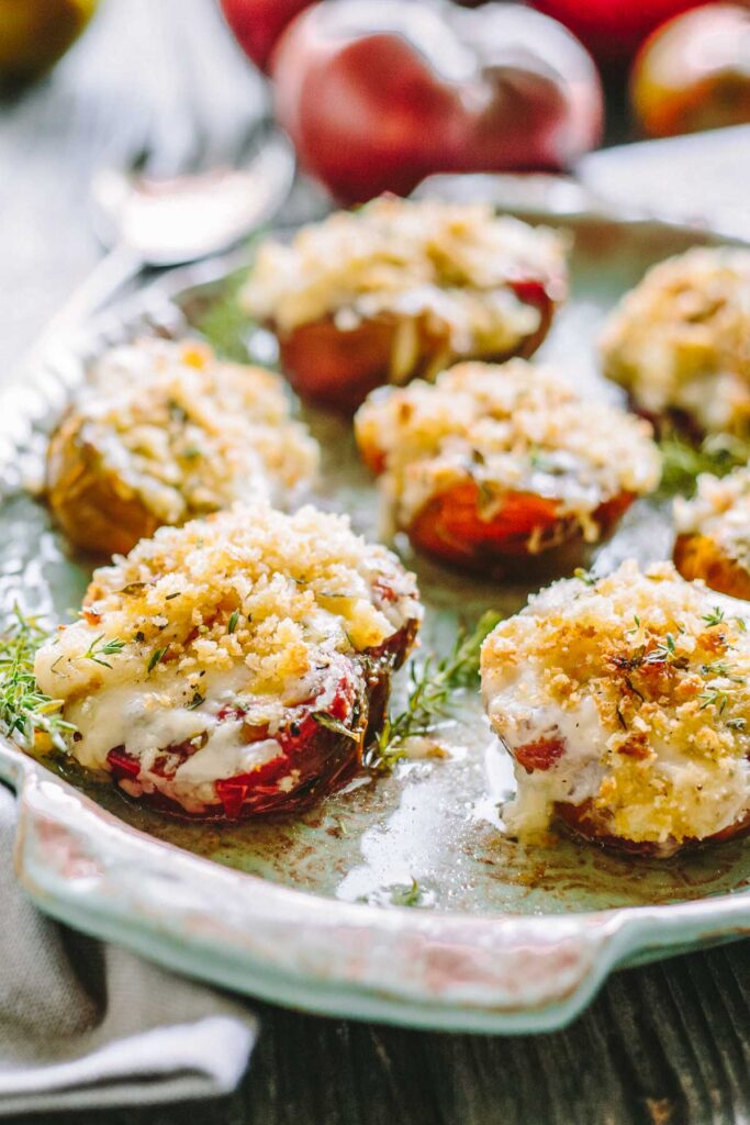 Zoomed-in shot of baked tomatoes covered in bubbly cheese and crispy panko, garnished with thyme on a decorative platter.