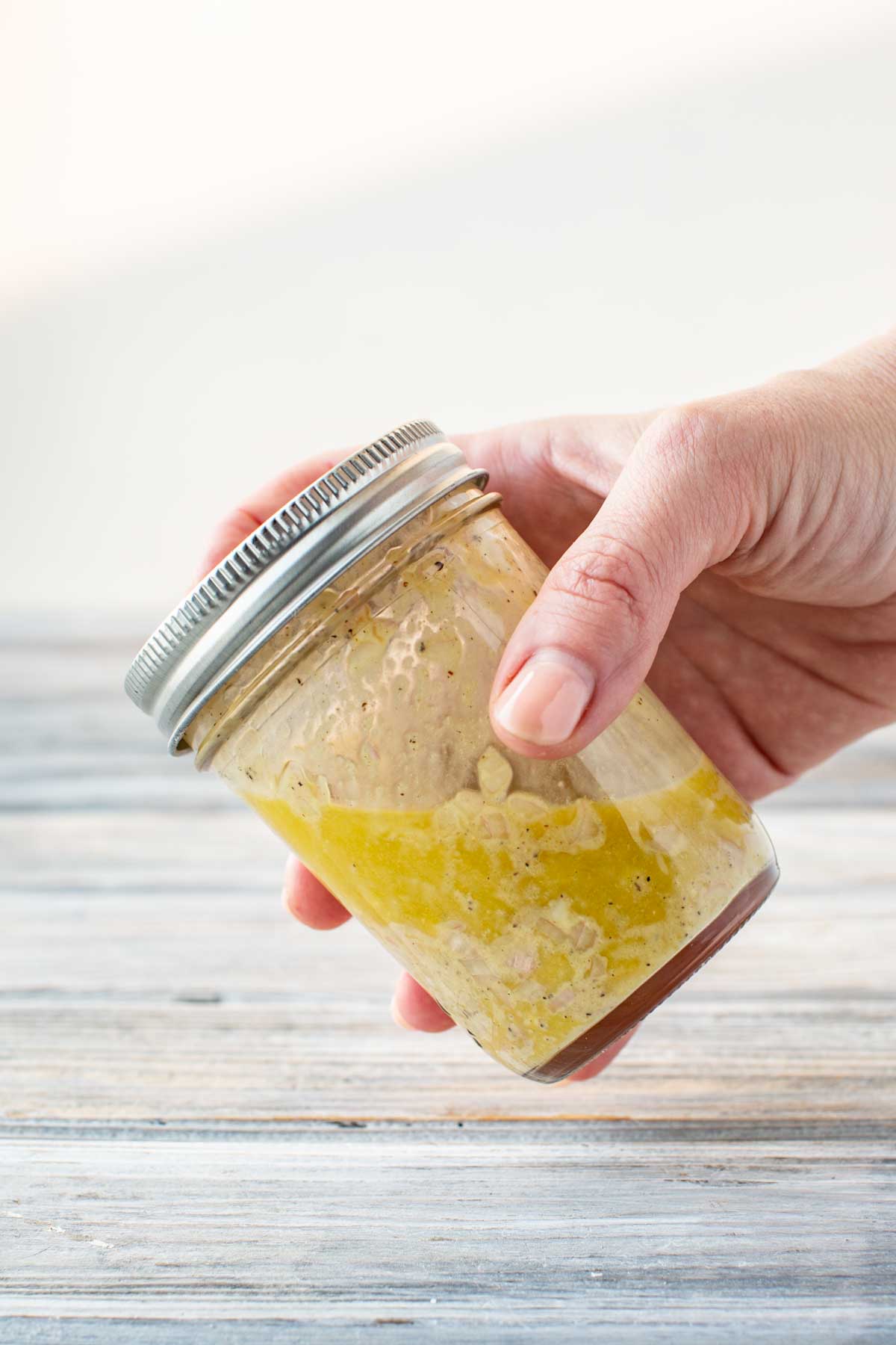 Hand holding a sealed mason jar filled with vinaigrette ingredients, ready to be shaken to emulsify the dressing.