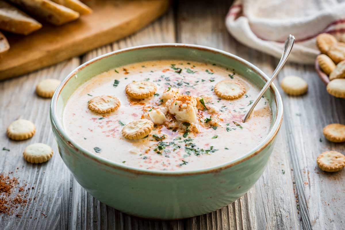 Creamy crab soup served in a green ceramic bowl, topped with oyster crackers, chopped herbs, and a sprinkle of paprika.