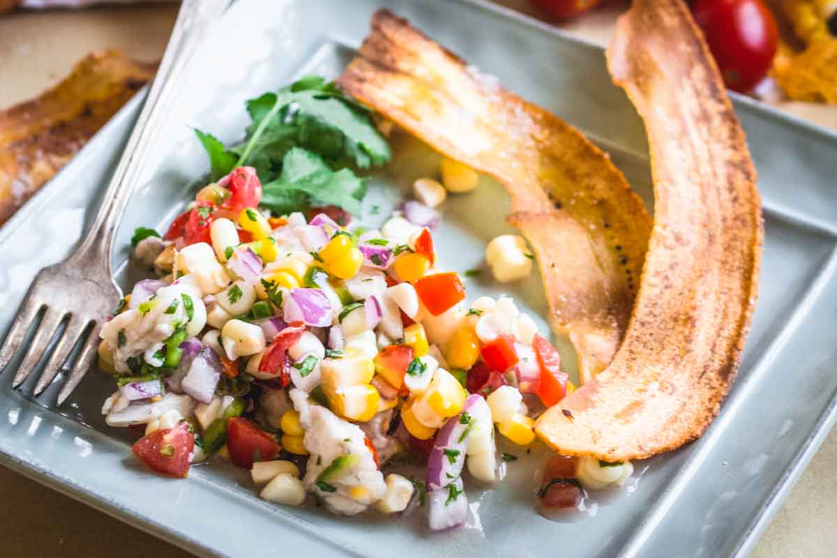Colorful ceviche served on a square plate with crispy plantain chips, garnished with cilantro and a vintage fork.