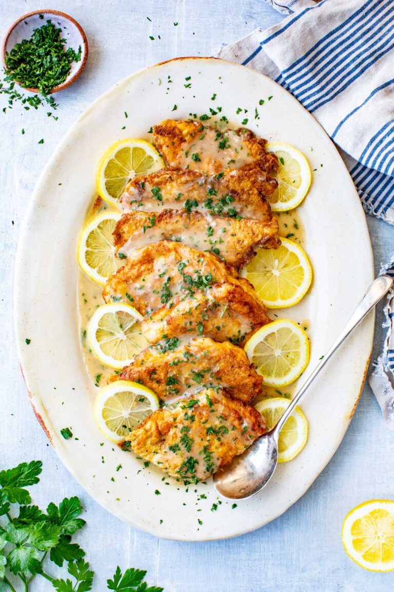 Breaded flounder francaise arranged over lemon slices on a white serving dish, topped with lemony butter sauce and fresh parsley.