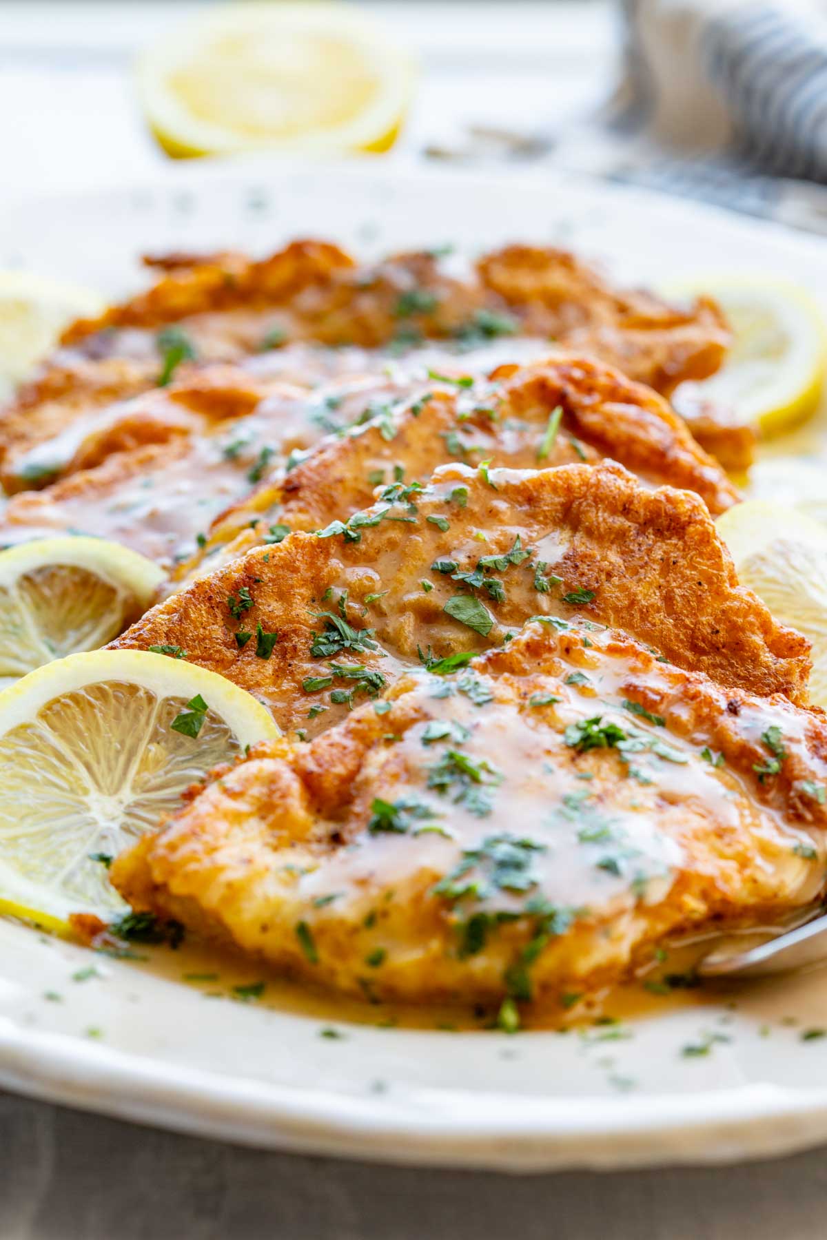 Side angle of flounder francaise on a large platter with visible lemon rounds and a generous coating of lemon-parsley sauce.