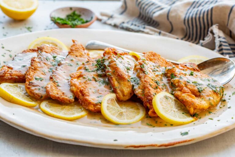 Close-up of crispy flounder francaise covered in silky lemon sauce, garnished with chopped parsley and lemon slices.