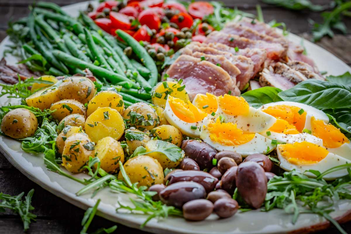 Angled close-up of herbed baby potatoes and soft-boiled eggs with olives, anchovies, and fresh tuna in the background.
