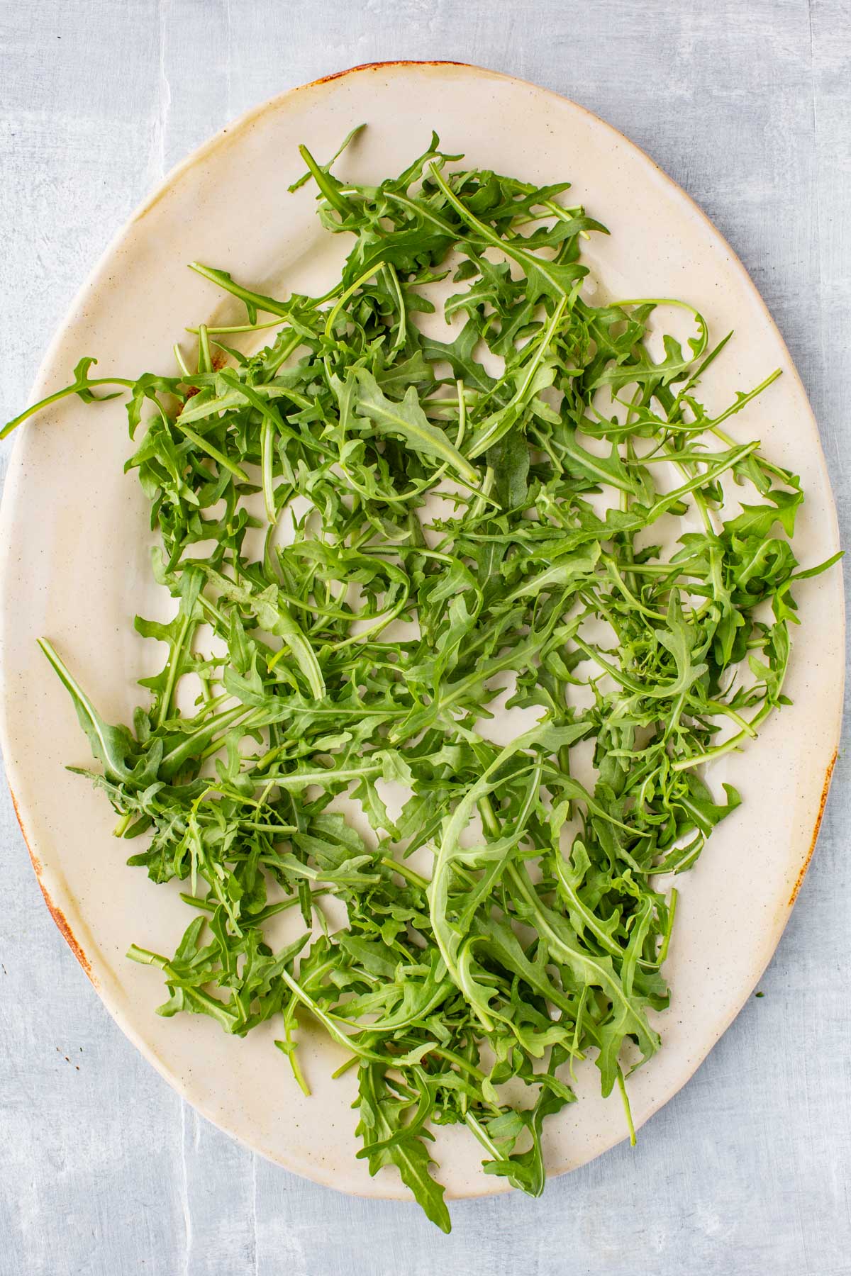 Oval platter filled with fresh arugula arranged as a bed for the composed Niçoise salad.