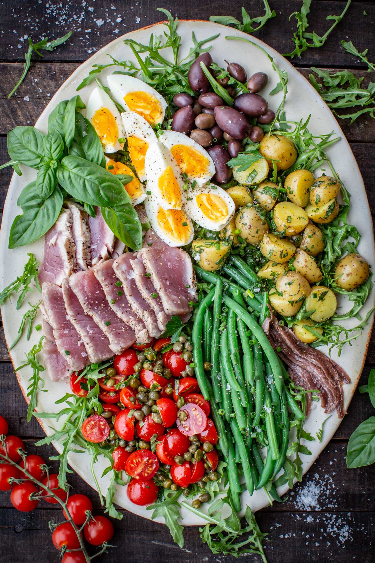 Colorful fresh tuna Niçoise salad styled on a rustic wood background with vibrant ingredients including green beans, potatoes, eggs, and tomatoes.
