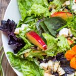 Crisp mixed salad greens with sliced nectarines, crumbled blue cheese, chopped nuts, and grilled corn in a white bowl.