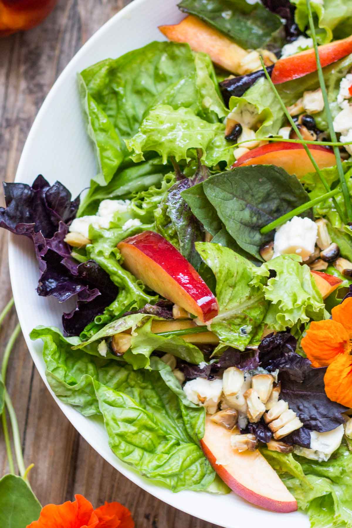 Crisp mixed salad greens with sliced nectarines, crumbled blue cheese, chopped nuts, and grilled corn in a white bowl.