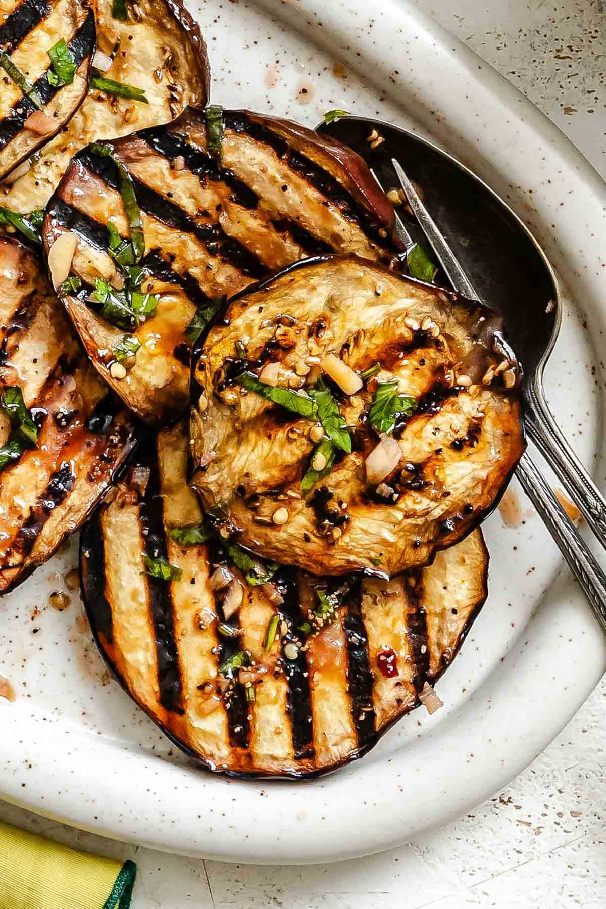 Tight shot showing texture of tender grilled eggplant slices topped with garlic, herbs, and dressing.