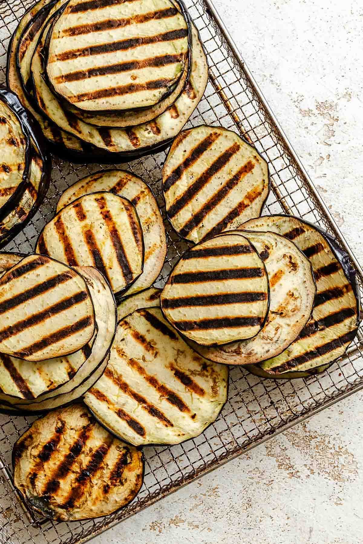 Eggplant slices with dark grill marks arranged on a wire rack to cool, showing a perfect sear.