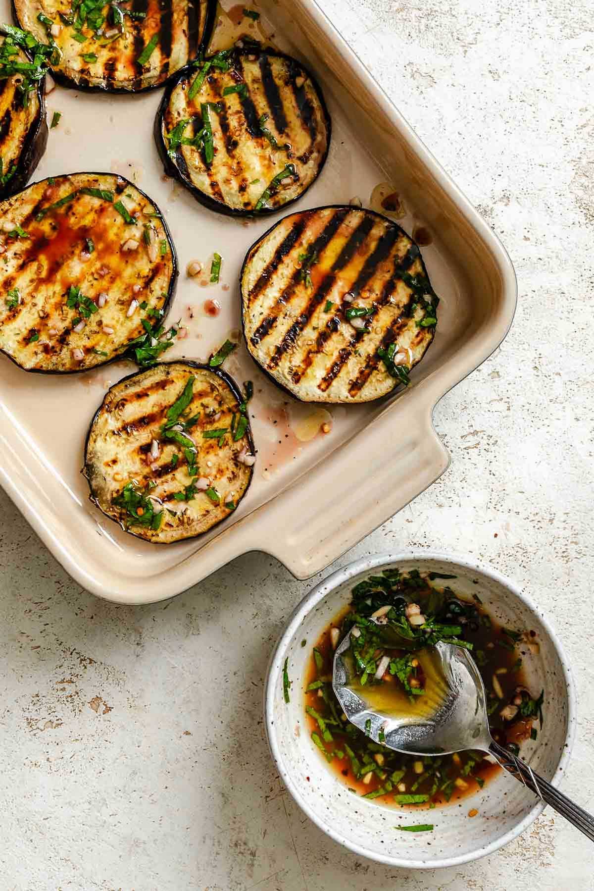 Grilled eggplant slices layered in a dish with the balsamic herb marinade spooned over top.