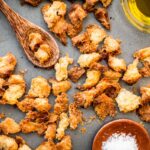 Overhead shot of baked croutons with sea salt and olive oil, and a wooden spoon holding a few pieces.