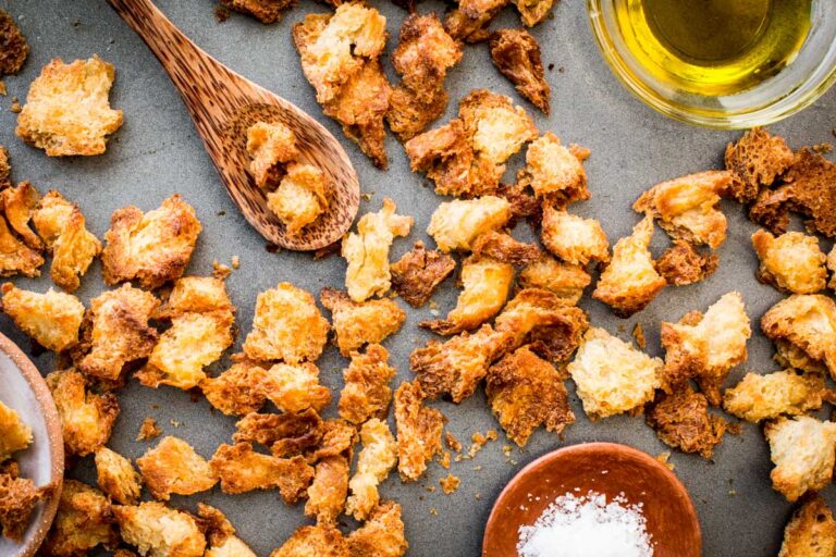 Overhead shot of baked croutons with sea salt and olive oil, and a wooden spoon holding a few pieces.