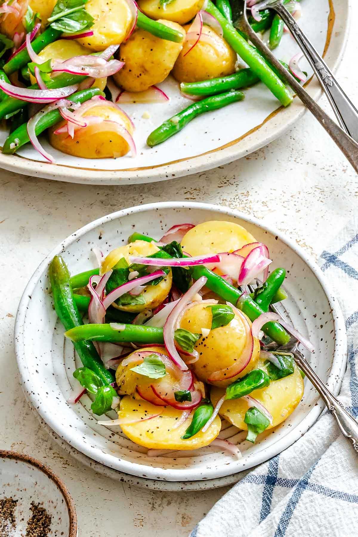 A portion of the potato salad served in a small speckled ceramic dish, garnished with fresh basil and cracked black pepper.