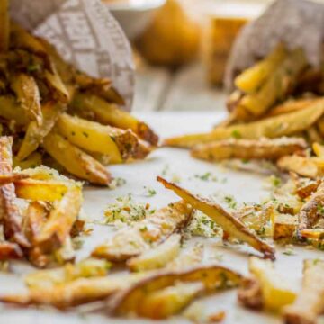 Golden brown truffle fries spilling out of paper cones, topped with grated Parmesan and chopped herbs.