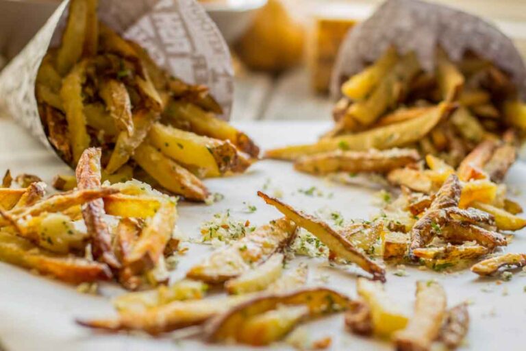 Golden brown truffle fries spilling out of paper cones, topped with grated Parmesan and chopped herbs.