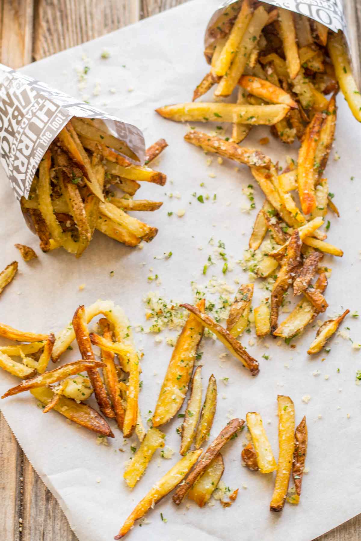 Overhead view of crispy Parmesan truffle fries scattered on parchment paper with paper cones and flecks of cheese and parsley.