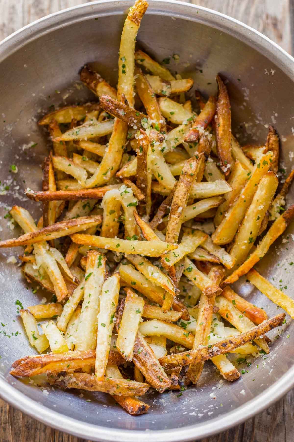 Close-up of freshly baked truffle fries in a stainless steel mixing bowl, coated with Parmesan cheese and herbs.