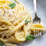 Close-up of pasta al limone with a fork twirling strands of spaghetti, garnished with basil and lemon zest on a stoneware plate.