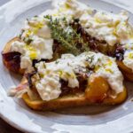 Plate of crostini with roasted plums and burrata, drizzled with olive oil and thyme sprigs for garnish, ready to serve.
