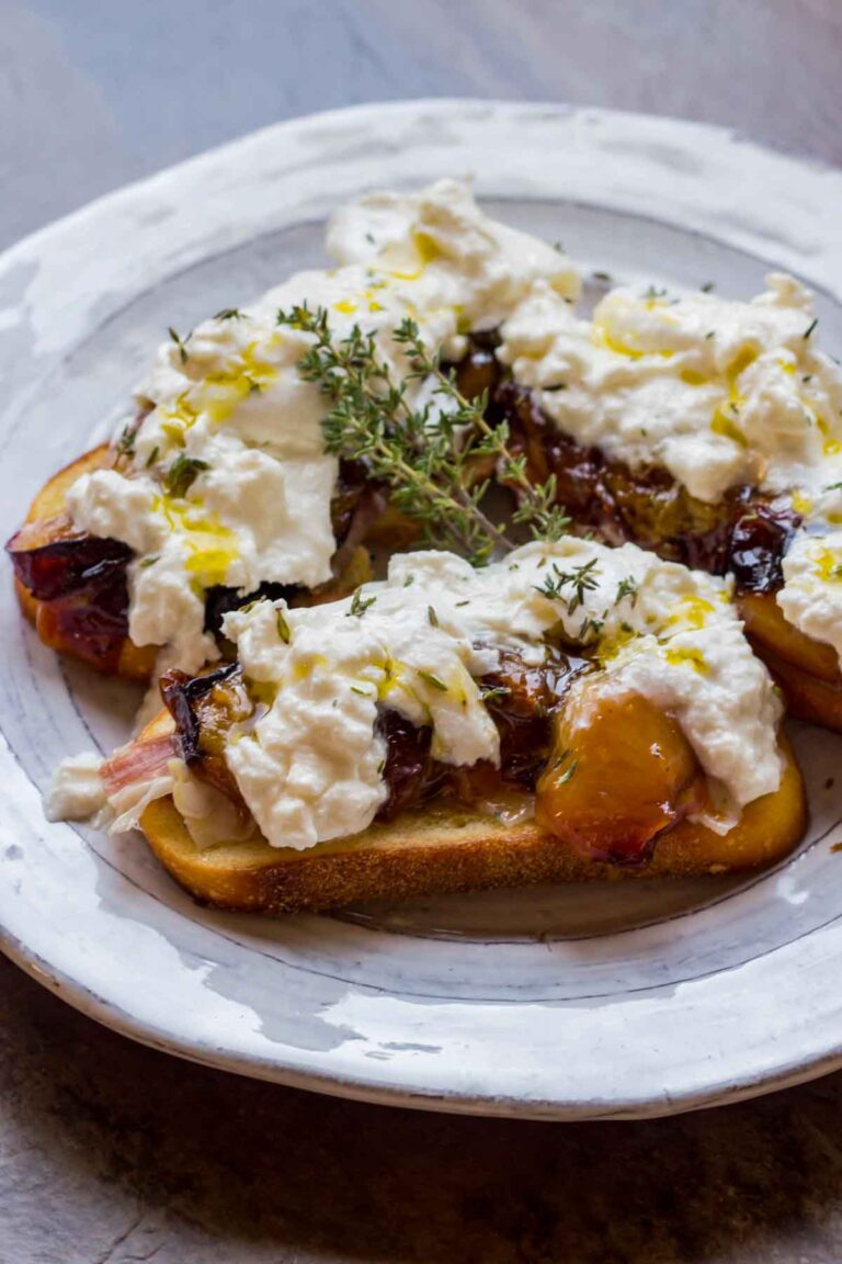 Plate of crostini with roasted plums and burrata, drizzled with olive oil and thyme sprigs for garnish, ready to serve.