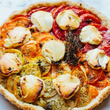 Fully baked tomato and goat cheese tart featuring blistered goat cheese rounds, vibrant heirloom tomatoes, and fresh herbs on a golden pastry crust.