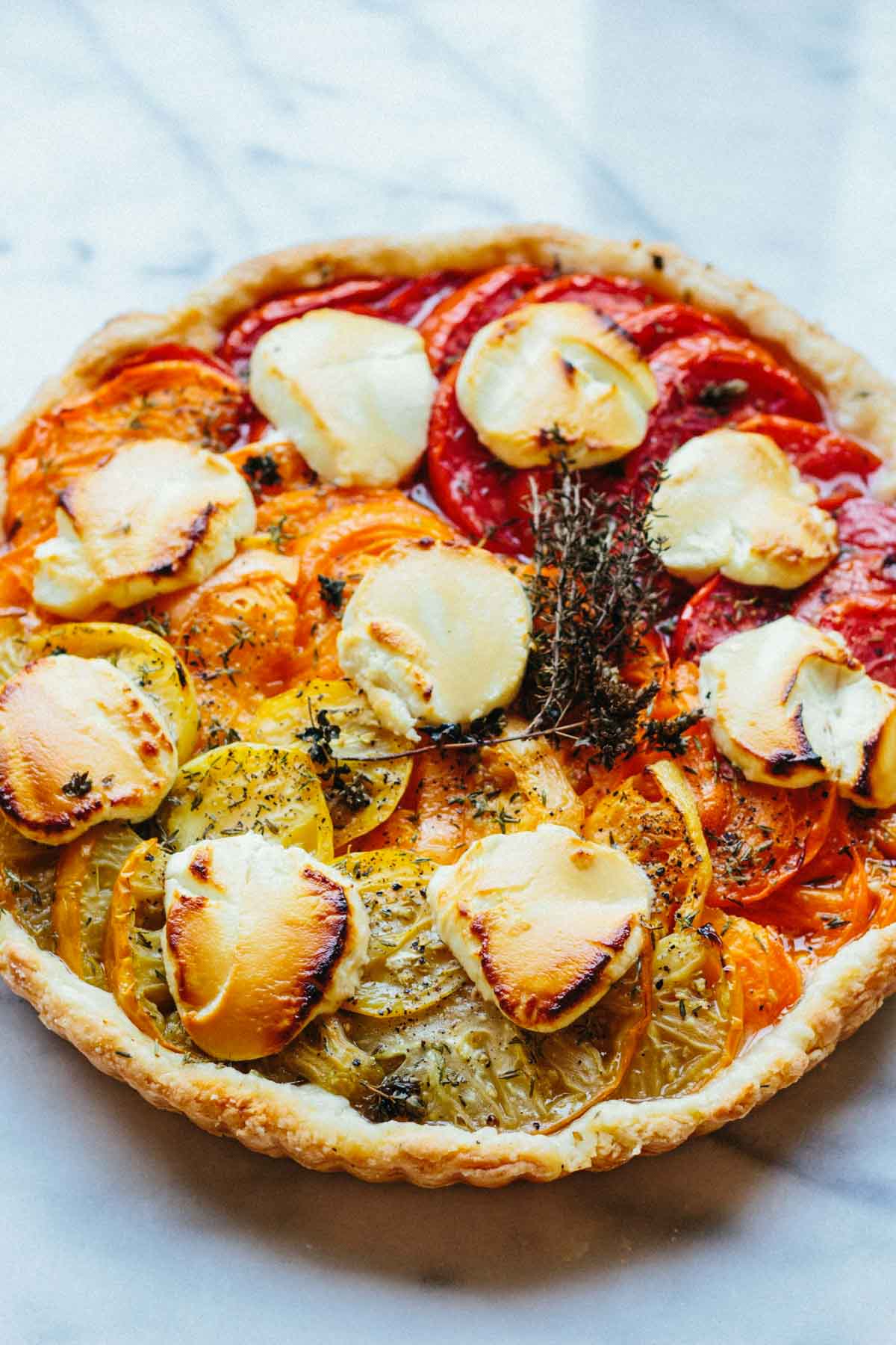 Fully baked tomato and goat cheese tart featuring blistered goat cheese rounds, vibrant heirloom tomatoes, and fresh herbs on a golden pastry crust.