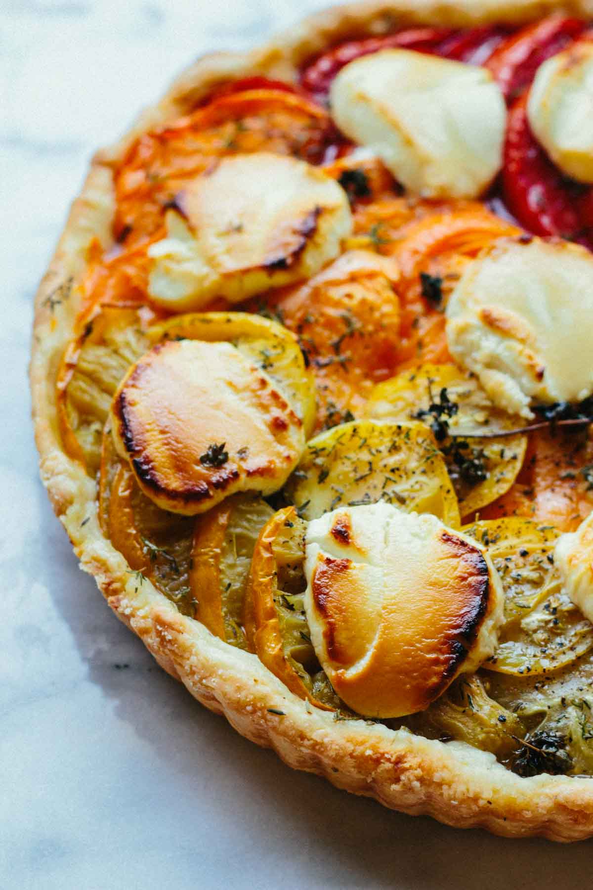 Close-up of the baked tomato goat cheese tart highlighting the caramelized edges of creamy goat cheese and the layered roasted heirloom tomatoes.