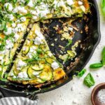 Close-up of the skillet showing missing slices and scattered bits of zucchini, feta, and basil over a crisped edge.