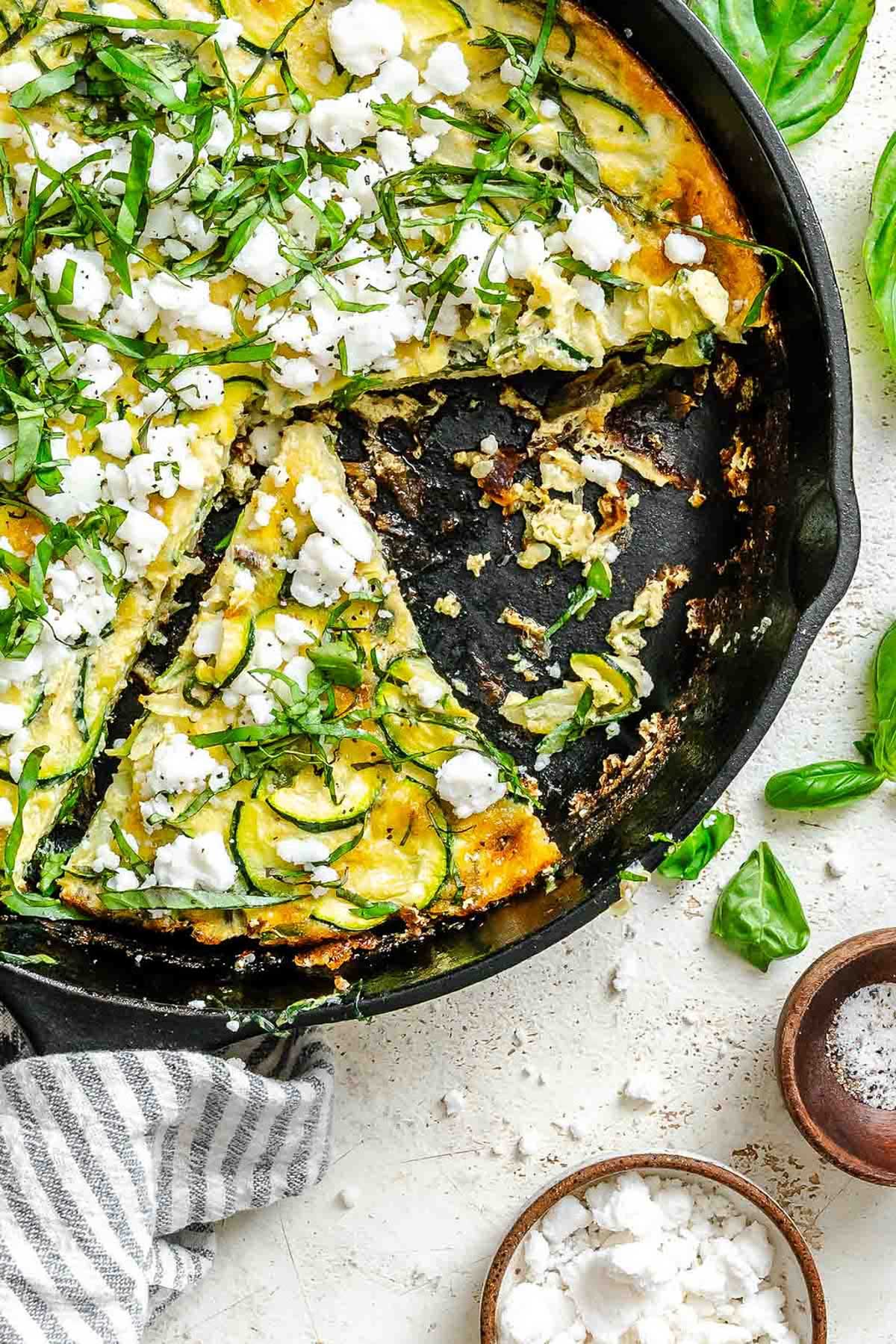 Close-up of the skillet showing missing slices and scattered bits of zucchini, feta, and basil over a crisped edge.