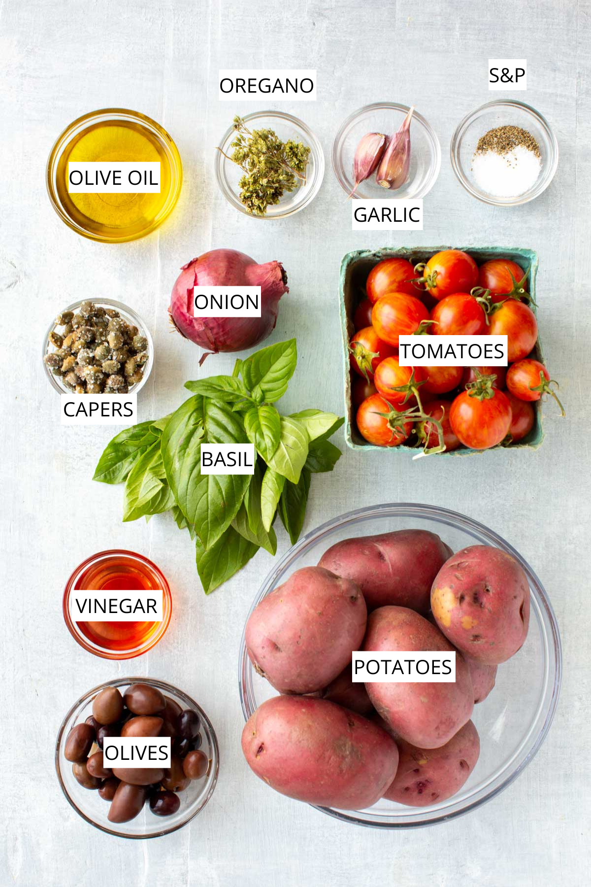 Ingredient layout - Overhead display of ingredients for insalata pantesca: olive oil, oregano, garlic, small red onion, cherry tomatoes, basil leaves, capers, vinegar, black olives, and medium red potatoes.