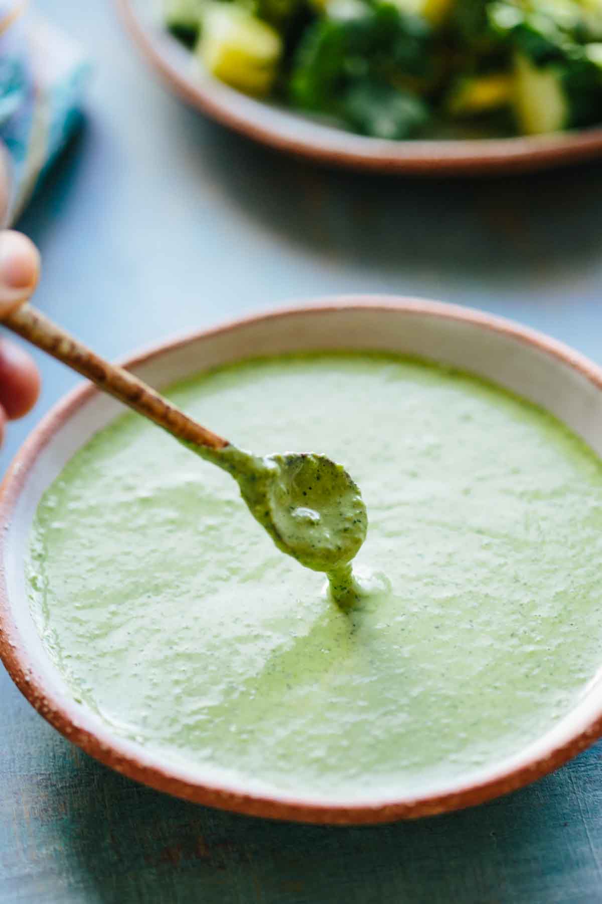 Bowl of Peruvian green sauce - A rustic bowl filled with smooth, creamy green sauce, with a spoon lifting some to show its velvety texture.