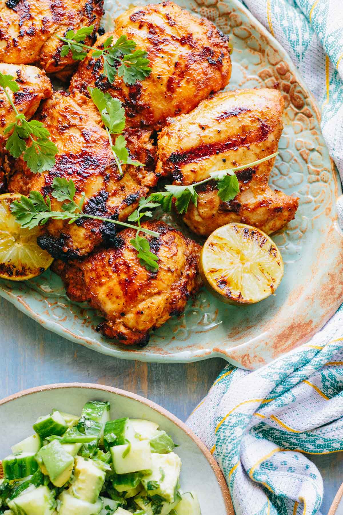 Platter of grilled chicken thighs with charred lime - Golden, smoky chicken thighs garnished with fresh cilantro sprigs and halved limes with grill marks, ready to be served.
