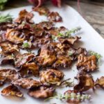 Rustic beet chips on parchment - Crispy oven-roasted beet chips scattered over parchment paper and garnished with fresh herbs on a wooden surface.