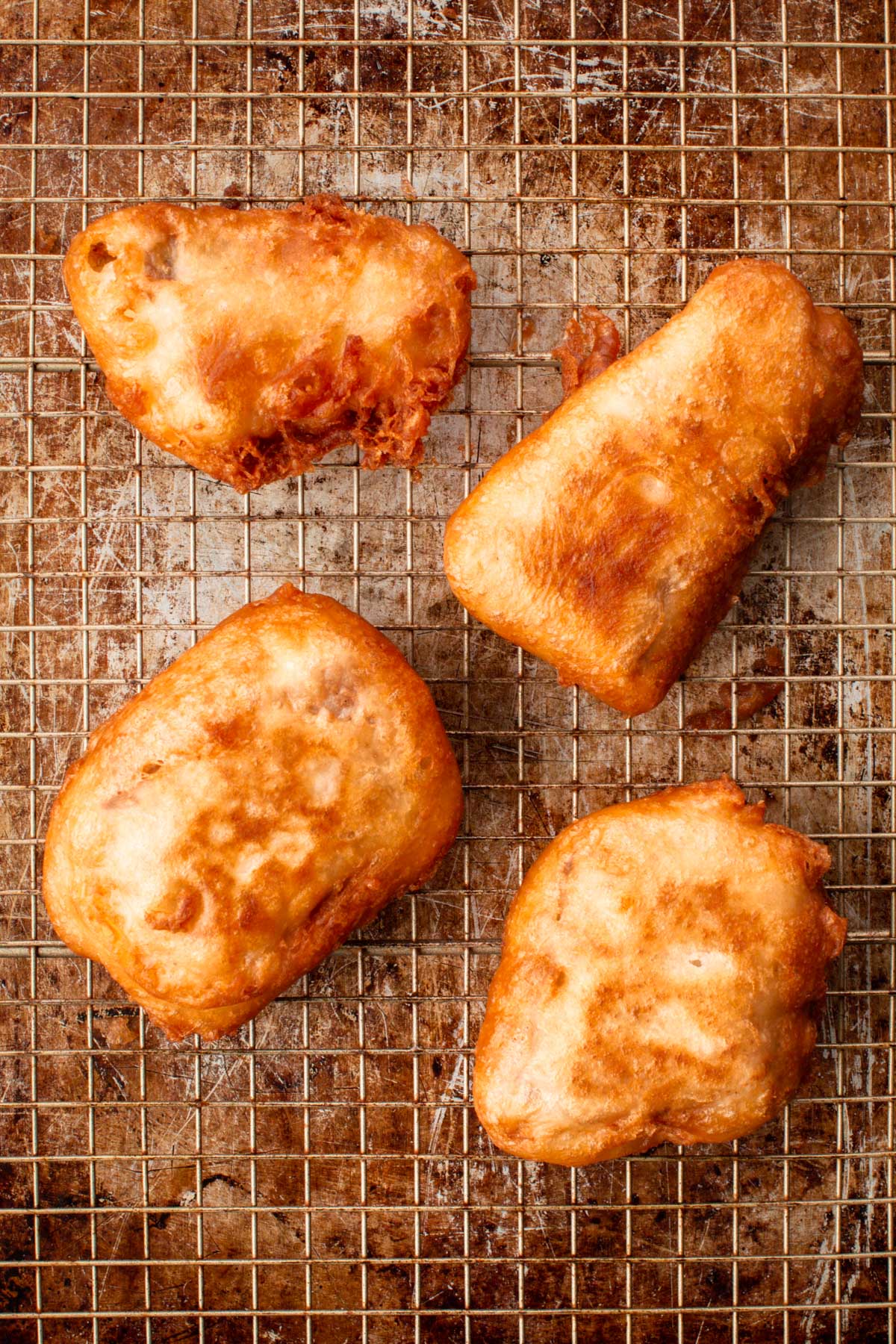 Four pieces of freshly fried beer-battered fish resting on a wire rack to drain excess oil.