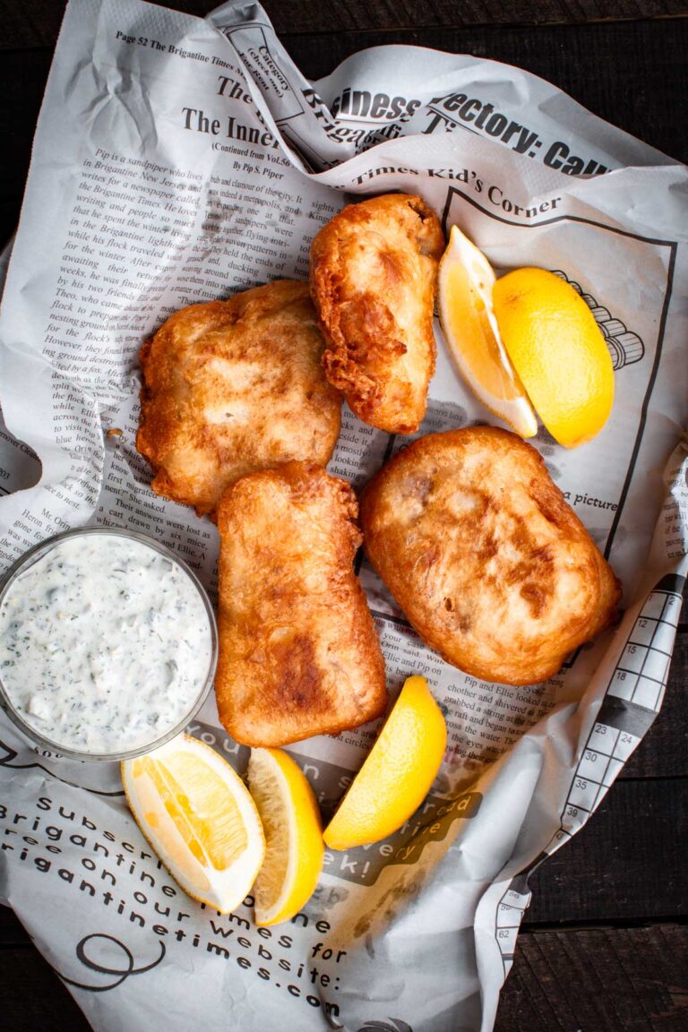 Overhead view of beer-battered fish served on newspaper with lemon wedges and tartar sauce.